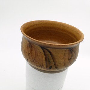 May include: A small, brown ceramic bowl with a decorative design of brown and black leaves. The bowl is slightly flared at the top and has a rounded bottom.