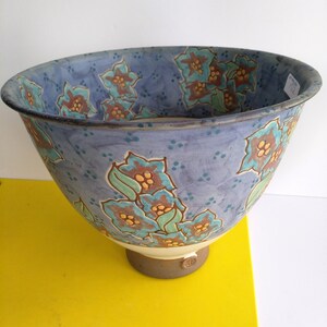 May include: A large, blue ceramic bowl with a floral design. The bowl has a wide rim and a rounded base. The flowers are painted in shades of blue, green, yellow, and brown.