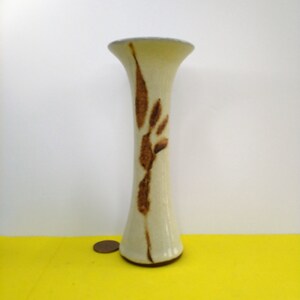 May include: A white ceramic vase with a brown leaf design. The vase has a narrow neck and a wide base.
