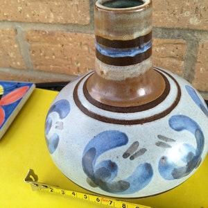 May include: A brown and blue ceramic vase with a white background and a floral design. The vase is approximately 18 cm tall.