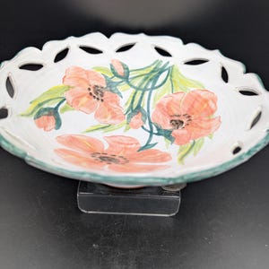 May include: White ceramic serving bowl with a scalloped edge and floral design. The bowl features hand-painted coral-colored poppies with green leaves and stems. The rim is trimmed with a green border.