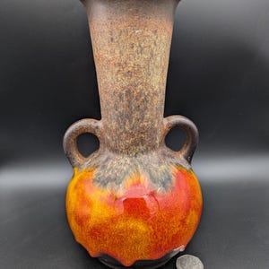 Könnte beinhalten: Eine braune und orangefarbene Keramikvase mit zwei Henkeln. Die Vase hat eine gefleckte Glasur in Braun-, Orange-, Rot- und Schwarztönen.