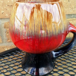 Peut inclure: Une tasse en céramique rouge, marron et noire avec un large bol rond et une anse. La tasse a un motif de glaçage unique en forme de gouttes.