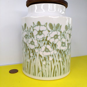 May include: White ceramic canister with a wood lid and a green and white floral pattern. The canister has a wide mouth and is perfect for storing dry goods.