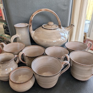 Può includere: Un set di tazze da tè e teiera in ceramica in una combinazione di colori crema e marrone. Il set comprende una teiera, un creamer e otto tazze.