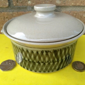 May include: A beige ceramic casserole dish with a lid. The dish has a green and brown geometric pattern.