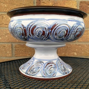 May include: A white ceramic pedestal bowl with a brown rim and blue and red swirl design.