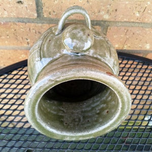 May include: A green ceramic planter with a rounded shape and a small handle on top. The planter has a glazed finish and a textured surface.