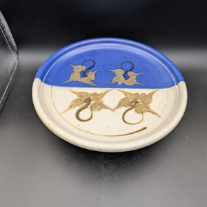 May include: A white ceramic plate with a blue rim and brown floral designs. The plate is divided in half, with the top half being blue and the bottom half being white.