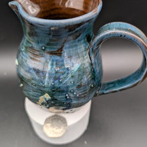 May include: A blue and brown ceramic pitcher with a white base. The pitcher has a speckled glaze and a rounded body.