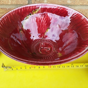 May include: A large, red ceramic bowl with a white and yellow glaze. The bowl has a decorative design on the bottom.