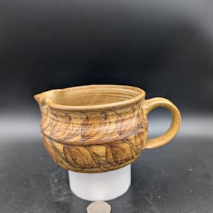 May include: A brown ceramic jug with a stylised leaf design. The jug has a rounded body and a handle.