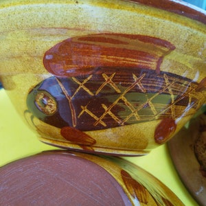 May include: Three ceramic bowls with a yellow, brown and red glaze. The bowls are decorated with a fish design. The fish has a brown body with a yellow and brown grid pattern and a red fin.
