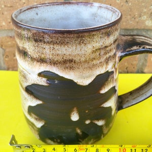 May include: A brown and white ceramic mug with a unique abstract design. The mug has a wide, rounded body and a handle.