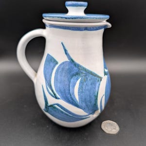May include: A white ceramic pitcher with a blue and white floral design and a lid. The pitcher has a handle and a spout.