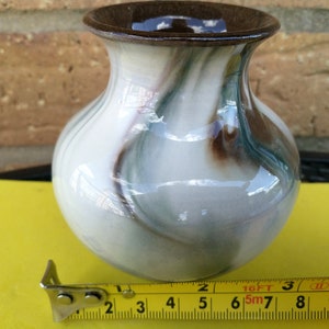 May include: A small, white ceramic vase with brown and green marbling. The vase is approximately 3 inches tall and has a round body.