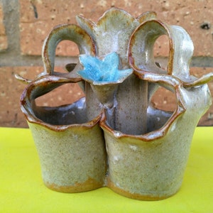 Peut inclure: Un pot en céramique avec trois compartiments distincts, chacun avec une forme unique et une surface rugueuse et texturée. Le pot est de couleur brun clair avec une fleur bleu clair au centre.