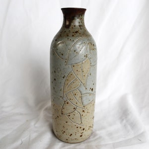 Może przedstawiać: Ceramiczny wazon z jasnoniebieską glazurą i brązowym, kropkowanym wykończeniem. Wazon ma wzór liści wyrzeźbionych w powierzchni.