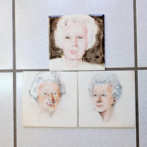 May include: Three watercolor paintings of women with white hair. The paintings are framed in white and are displayed on a white tiled wall.