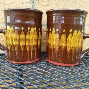 May include: Two brown ceramic mugs with a yellow and brown pattern. The mugs have a rounded shape and a handle.