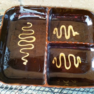 May include: A brown ceramic serving dish with three sections. Each section has a decorative swirl design in a light yellow color.