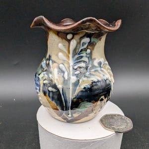 May include: A small, hand-painted ceramic vase with a scalloped rim. The vase features a blue, white, and brown floral design.
