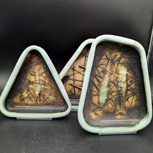 May include: Three ceramic dishes with a fish skeleton design. Each dish has a black and brown background with a light blue border. The fish skeleton is in a light blue color. The dishes are on clear plastic stands.