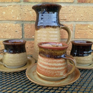 May include: Set of four brown and tan ceramic mugs with a brown and tan ceramic jug. The mugs and jug have a rustic, handmade look.