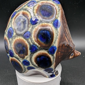 May include: A ceramic hedgehog figurine with a brown and white base and blue and white spots.