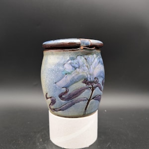 Op de afbeelding: Een blauwe en witte keramische pot met een bloemenmotief en een scharnierend deksel. De pot heeft een bruine rand en een witte basis.