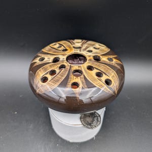 May include: A brown ceramic flower frog with a decorative design in shades of brown and gold. The frog has multiple holes for holding flower stems.