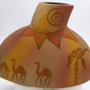 Peut inclure: Un vase en céramique avec une base large et arrondie et un col étroit. Le vase est décoré d'un soleil stylisé, d'un palmier et de trois chameaux dans un paysage désertique. Les couleurs sont orange, jaune et marron.