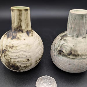 May include: Two small ceramic vases with a textured surface and a mottled glaze in shades of white, green, and brown.