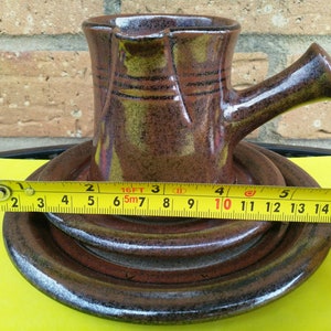 May include: A brown ceramic pitcher with a handle and a matching saucer. The pitcher is 6.5 inches tall and the saucer is 10 inches in diameter.