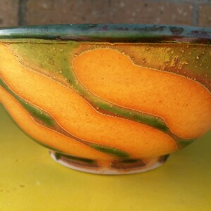 May include: A ceramic bowl with a yellow glaze and green and brown accents. The bowl has a wavy pattern.