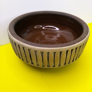 Peut inclure: Un bol en céramique brun avec un bord blanc et des lignes verticales autour de l'extérieur. Le bol est vide.