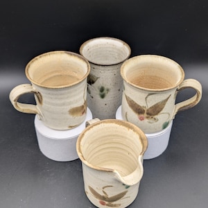 Può includere: Set di quattro tazze in ceramica con una glassa color crema e disegni di farfalle marroni e verdi. Le tazze sono fatte a mano e hanno un aspetto rustico.