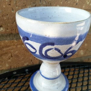 May include: A white ceramic goblet with a blue and white design. The goblet has a wide bowl and a tall stem.
