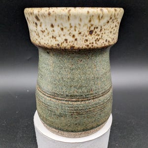 May include: A ceramic vase with a speckled white and brown glaze on the top and a green glaze with brown stripes on the bottom.