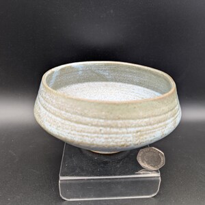 May include: A handcrafted ceramic bowl with a wide, shallow design. The bowl has a light blue and beige colour scheme with a textured, layered appearance. The bowl is approximately 15 cm in diameter.