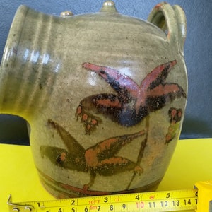 May include: A green ceramic jug with a spout and a handle. The jug has a brown and red floral design painted on the side.