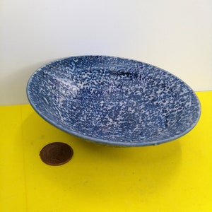 May include: A small, blue and white speckled ceramic bowl. The bowl is shallow and has a rounded shape.