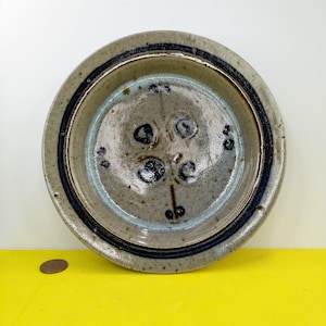 Może przedstawiać: Ceramiczny talerz z niebieskim i brązowym wzorem. Talerz ma kwiatowy wzór w środku i niebieski brzeg.