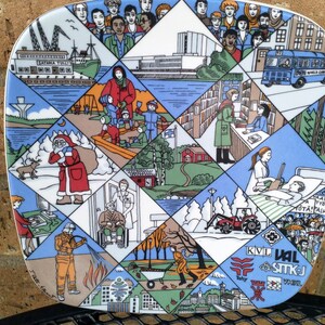 May include: A colorful ceramic plate with a diamond pattern design. Each diamond features a different scene, including a winter scene with a man in a red suit, a city scene with buildings and a bus, and a forest scene with trees and a river. The plate has the text "KVL VAL STIKJ" in the lower right corner.