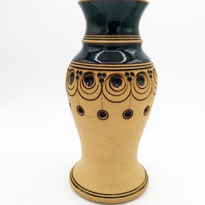 Könnte beinhalten: Eine Keramikvase mit einem schwarzen und gelben Design. Die Vase hat eine breite Öffnung und einen schmalen Boden. Sie ist mit einem geometrischen Muster aus Kreisen und Linien verziert.