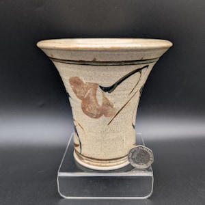 May include: A handmade ceramic vase with a flared top and a speckled, beige finish. The vase features brown and black abstract floral designs. The vase is approximately 5 inches tall and 6 inches wide at the top.