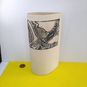 May include: A white ceramic vase with a black and grey abstract design. The vase has a rounded shape and a slightly curved top.