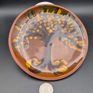 May include: A brown ceramic plate with a tree design painted in yellow, green, and brown. The tree has a thick trunk and branches with small yellow circles representing fruit.