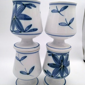 May include: Set of four white ceramic cups with blue floral designs. The cups have a pedestal base and are stacked in pairs.