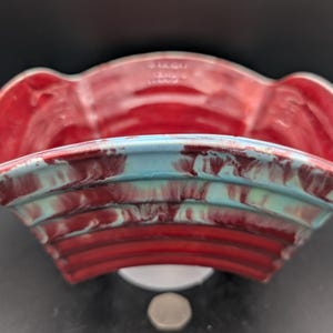 Può includere: Un vaso da fiori in ceramica rosso e blu con un design ondulato. Il vaso ha un bordo a festoni ed è fatto di ceramica smaltata.